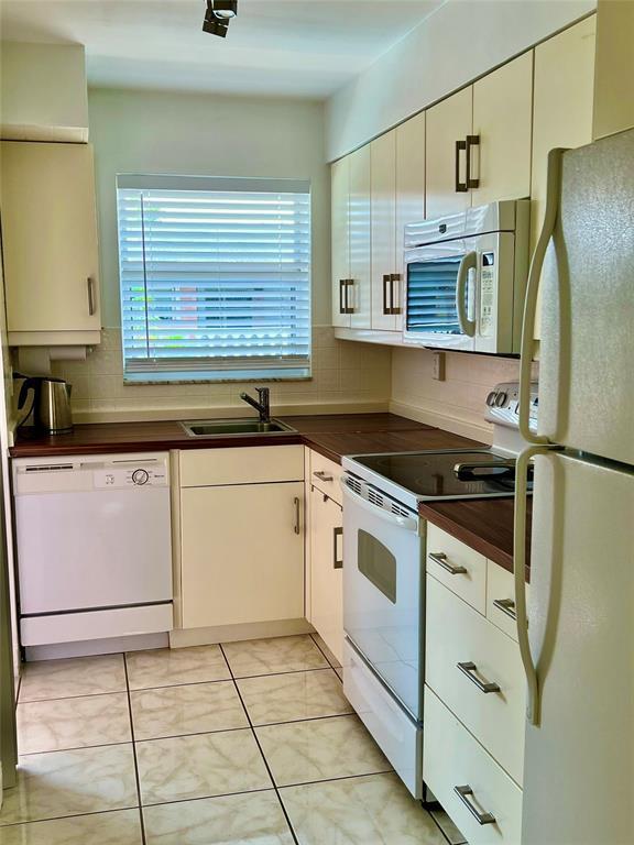 kitchen featuring decorative backsplash, sink, light tile patterned floors, and white appliances