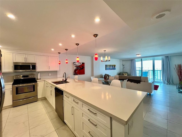 kitchen with kitchen peninsula, appliances with stainless steel finishes, sink, pendant lighting, and white cabinetry