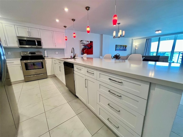 kitchen with kitchen peninsula, sink, stainless steel appliances, and decorative light fixtures