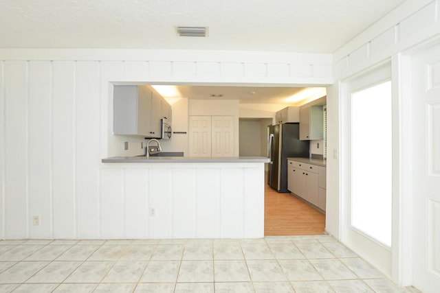 kitchen with kitchen peninsula, stainless steel fridge, sink, and white cabinets