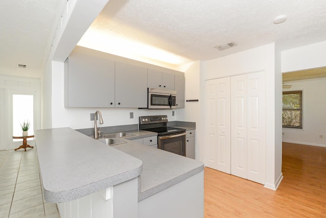 kitchen with sink, kitchen peninsula, a textured ceiling, gray cabinets, and appliances with stainless steel finishes