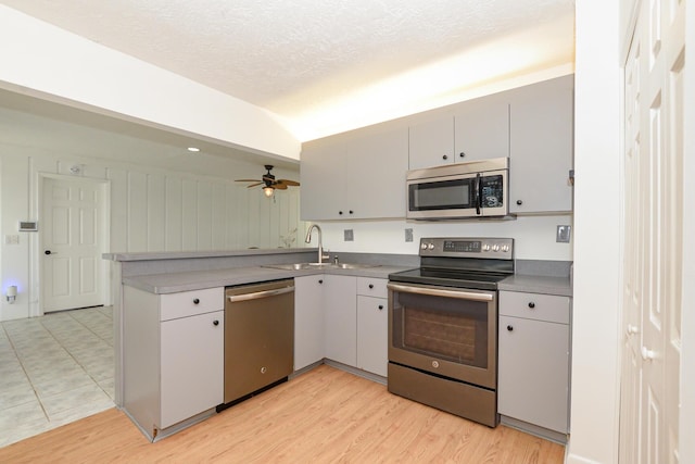 kitchen featuring kitchen peninsula, a textured ceiling, stainless steel appliances, ceiling fan, and sink