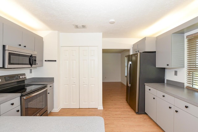 kitchen with appliances with stainless steel finishes, a textured ceiling, light hardwood / wood-style floors, and gray cabinets