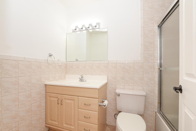 full bathroom featuring combined bath / shower with glass door, vanity, toilet, and tile walls