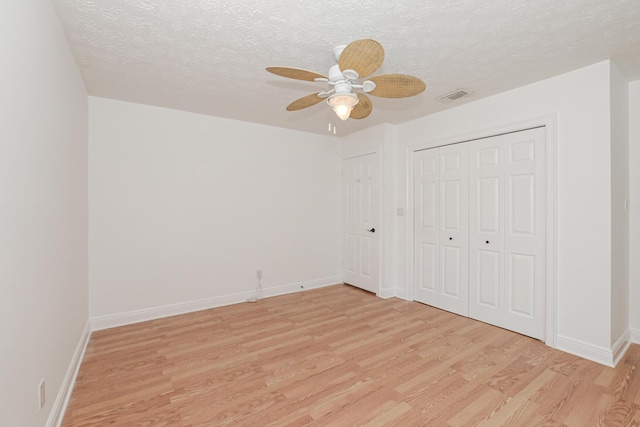 unfurnished bedroom featuring a textured ceiling, a closet, light hardwood / wood-style flooring, and ceiling fan