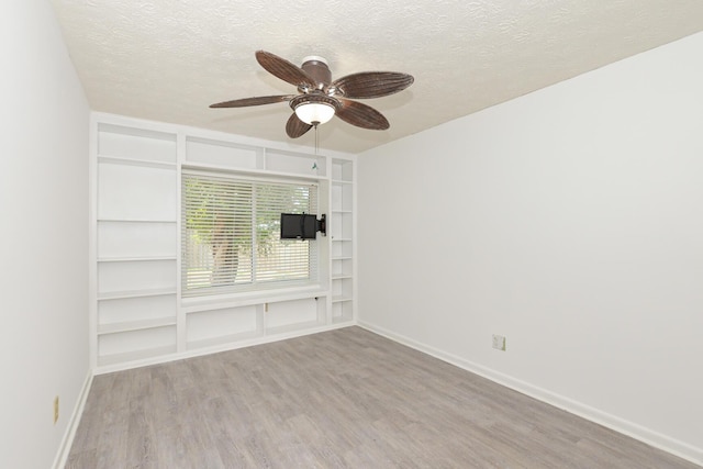 empty room with built in shelves, ceiling fan, light hardwood / wood-style flooring, and a textured ceiling