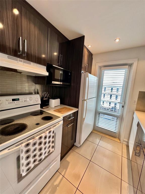 kitchen with dark brown cabinetry, white appliances, backsplash, and light tile patterned floors