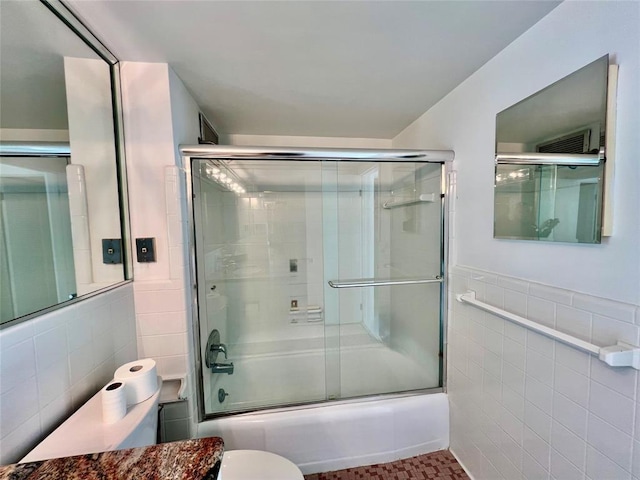 bathroom with tile patterned floors, toilet, tile walls, and bath / shower combo with glass door