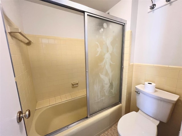 bathroom with tile patterned floors, toilet, tile walls, and bath / shower combo with glass door