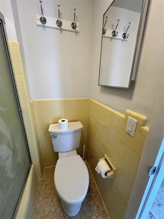 bathroom featuring shower / bath combination with glass door, tile patterned floors, toilet, and tile walls