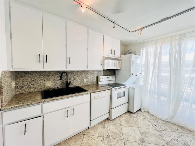 kitchen featuring white cabinetry, sink, stacked washer / dryer, track lighting, and white appliances