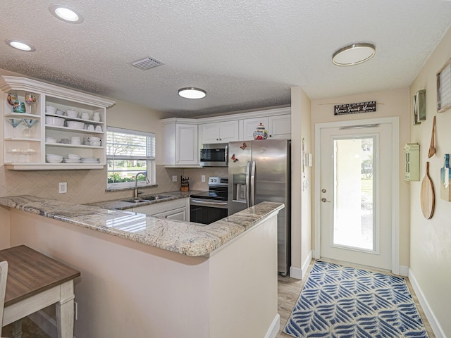 kitchen featuring sink, a kitchen breakfast bar, kitchen peninsula, white cabinets, and appliances with stainless steel finishes