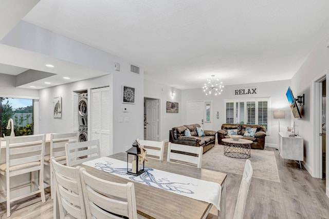 dining room with stacked washing maching and dryer, an inviting chandelier, and light wood-type flooring