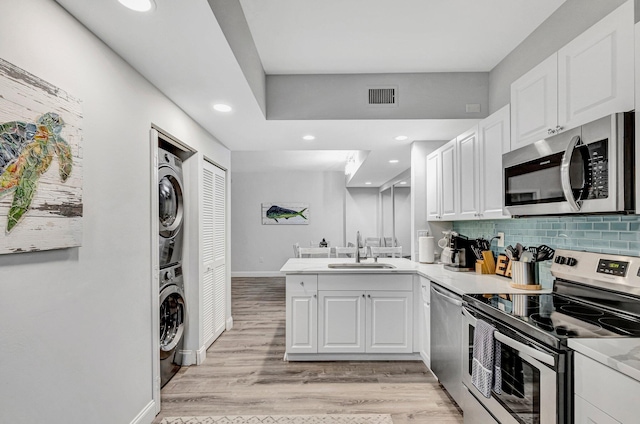 kitchen with sink, appliances with stainless steel finishes, white cabinetry, and stacked washer / drying machine