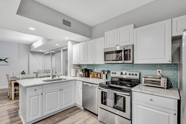 kitchen with appliances with stainless steel finishes, kitchen peninsula, light stone countertops, sink, and white cabinetry