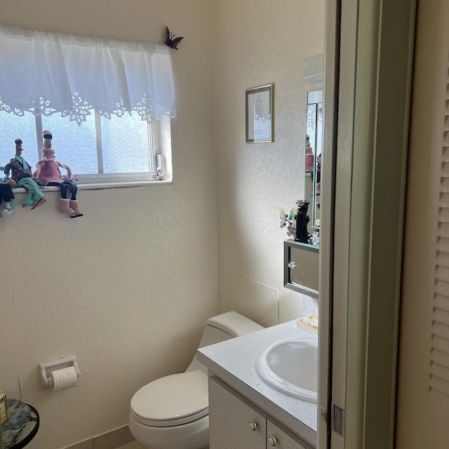 half bath with a textured wall, vanity, and toilet