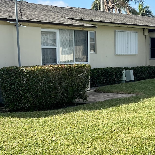 view of side of home featuring a shingled roof, a lawn, and stucco siding