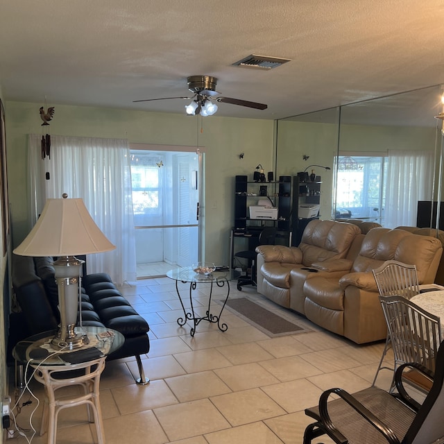 living room with a textured ceiling, light tile patterned flooring, visible vents, and a ceiling fan