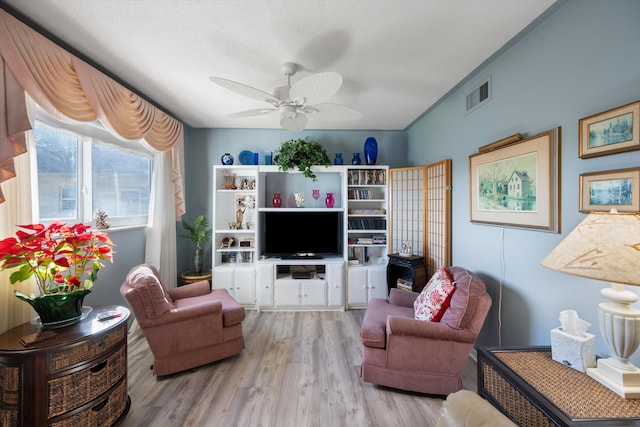 living room featuring ceiling fan, light wood-type flooring, and a textured ceiling