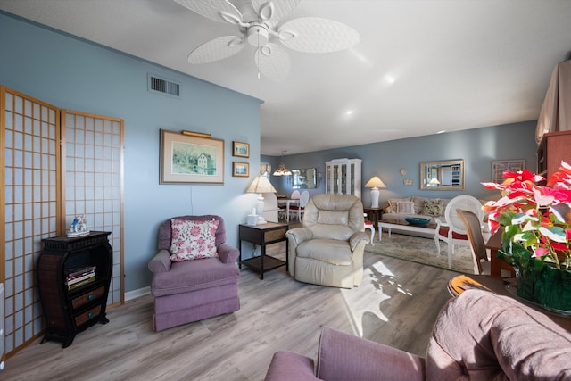 living room featuring ceiling fan with notable chandelier and light hardwood / wood-style flooring