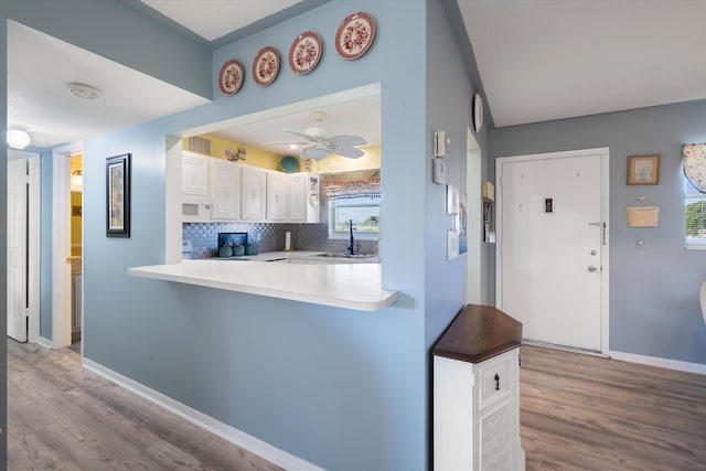 kitchen with decorative backsplash, kitchen peninsula, ceiling fan, sink, and white cabinetry