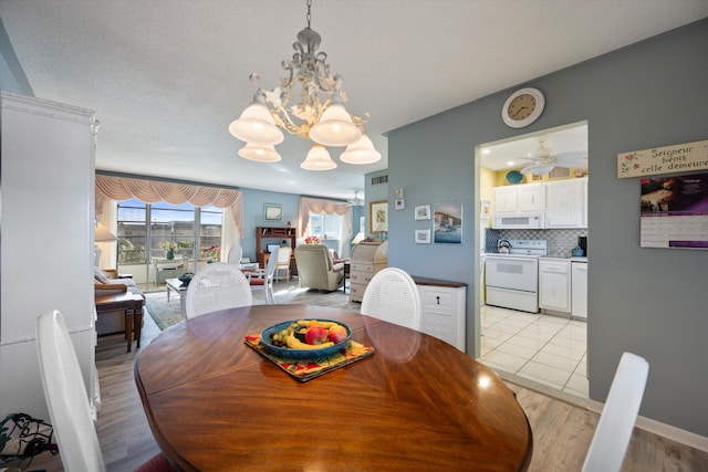 dining room featuring ceiling fan with notable chandelier and light hardwood / wood-style floors