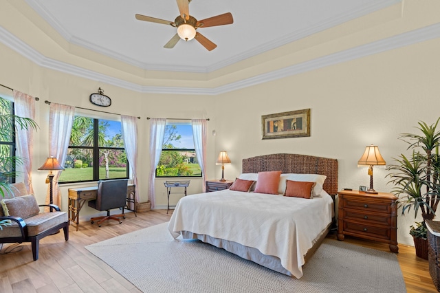 bedroom with light wood-type flooring, ceiling fan, ornamental molding, and a raised ceiling