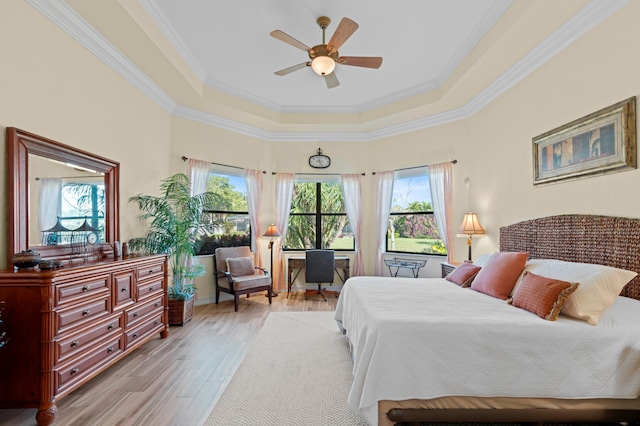 bedroom featuring ceiling fan, a tray ceiling, crown molding, and light wood-type flooring