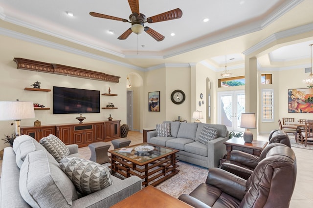 living room featuring ceiling fan with notable chandelier, a tray ceiling, crown molding, and light tile patterned flooring