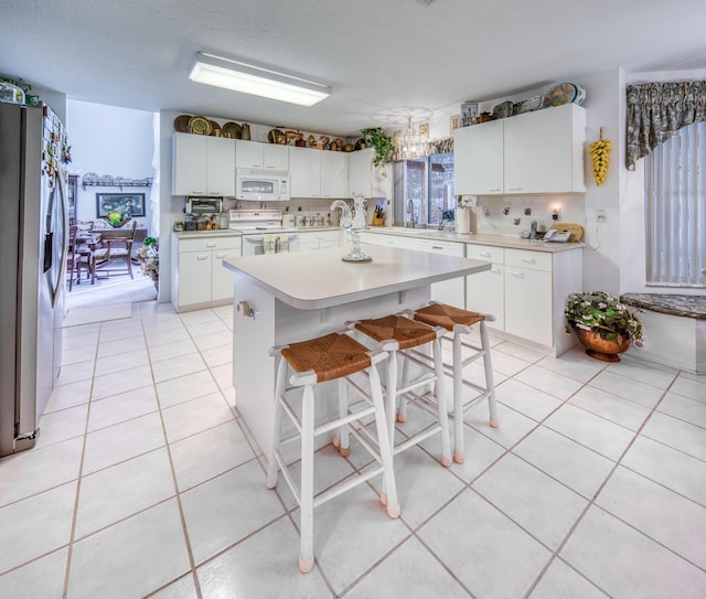 kitchen with white appliances, white cabinetry, an island with sink, decorative backsplash, and a kitchen breakfast bar