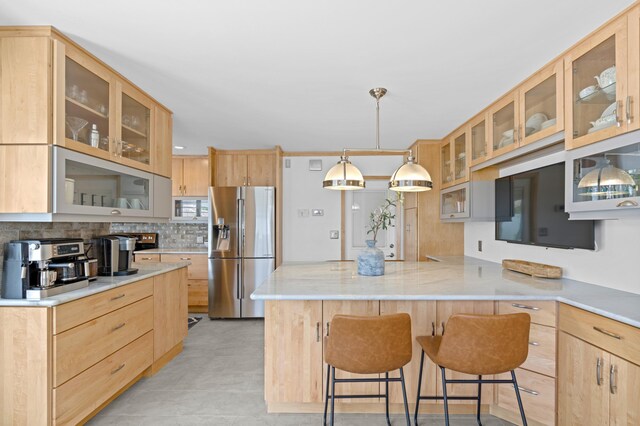 kitchen with a kitchen breakfast bar, hanging light fixtures, kitchen peninsula, light stone countertops, and light brown cabinets