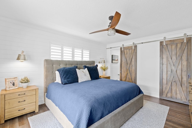 bedroom featuring ceiling fan, a barn door, and dark hardwood / wood-style flooring