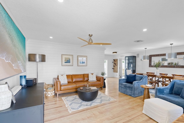 living room featuring ornamental molding, a textured ceiling, ceiling fan, and light hardwood / wood-style flooring