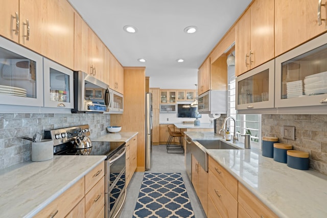 kitchen with light brown cabinetry, tasteful backsplash, sink, light stone counters, and stainless steel appliances