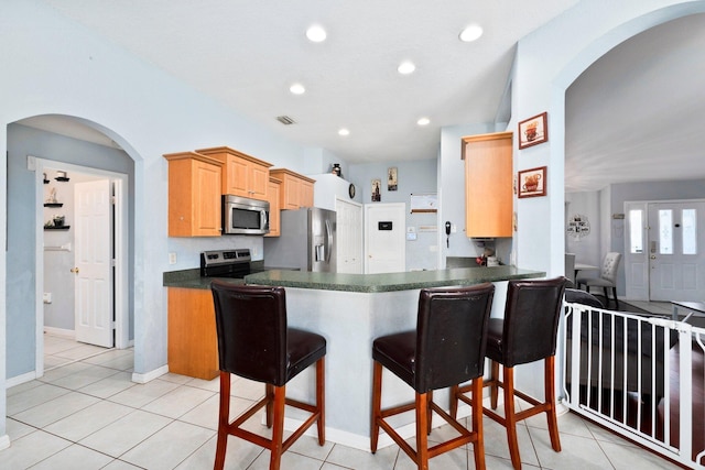 kitchen featuring light brown cabinets, light tile patterned flooring, kitchen peninsula, and appliances with stainless steel finishes