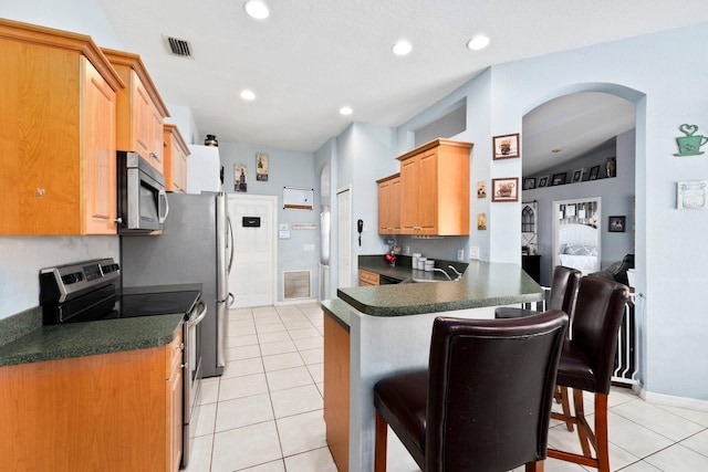 kitchen with kitchen peninsula, appliances with stainless steel finishes, light tile patterned flooring, and a breakfast bar area