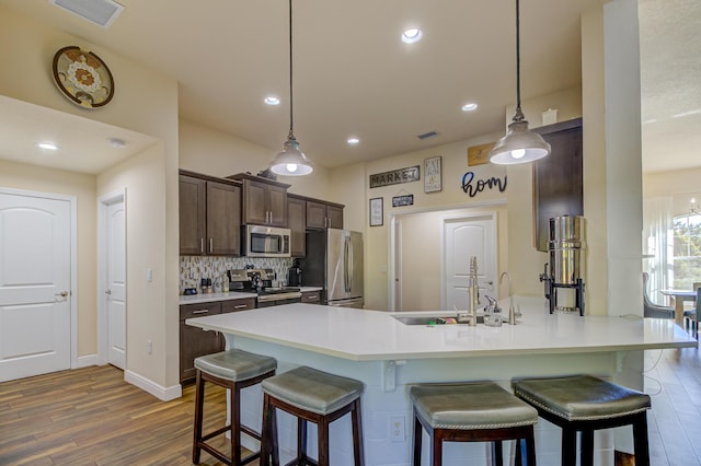 kitchen with a breakfast bar, dark brown cabinetry, hanging light fixtures, and appliances with stainless steel finishes