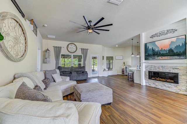 living room featuring ceiling fan, a fireplace, dark hardwood / wood-style floors, and a textured ceiling