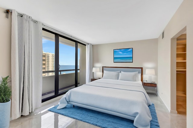 tiled bedroom with access to outside, a closet, a walk in closet, a water view, and expansive windows