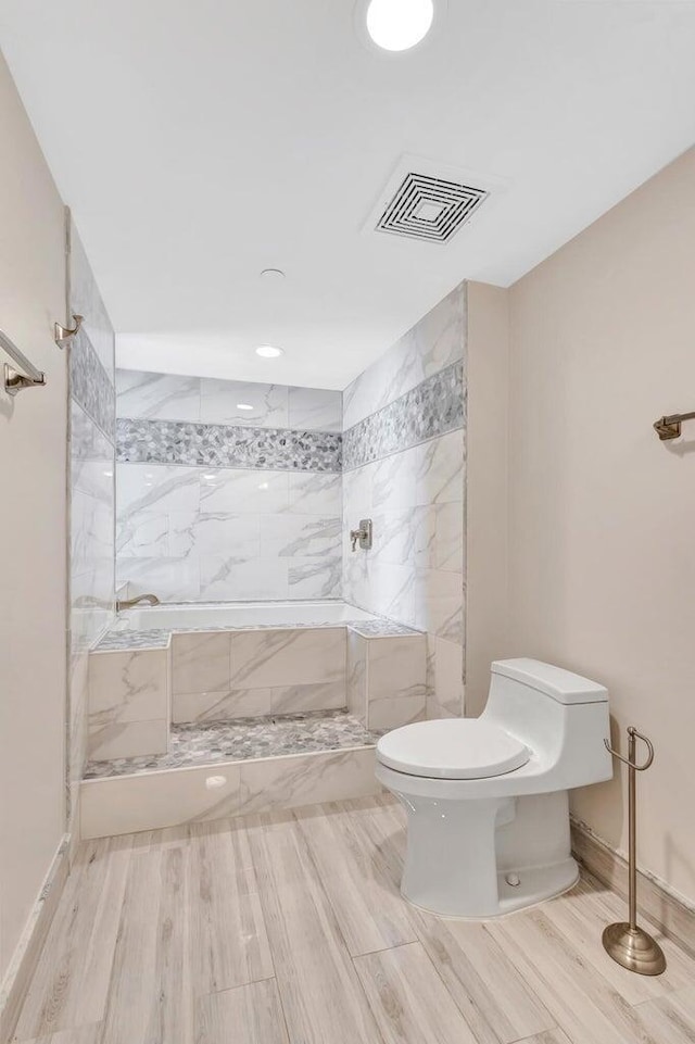 bathroom with toilet, tiled shower, and hardwood / wood-style floors