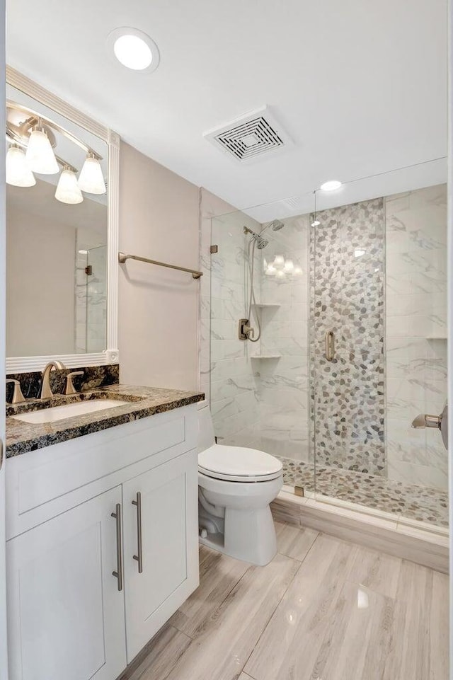 bathroom featuring a shower with door, toilet, and vanity