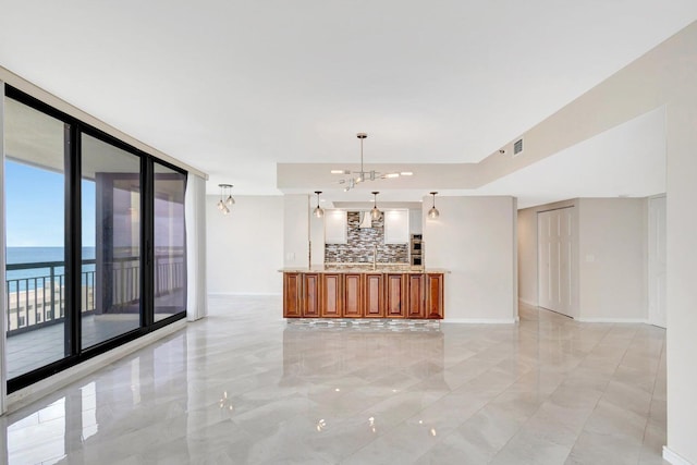 kitchen with tasteful backsplash, pendant lighting, an inviting chandelier, a water view, and a wall of windows