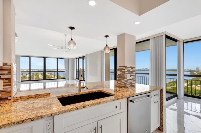 kitchen featuring dishwasher, sink, hanging light fixtures, a water view, and expansive windows