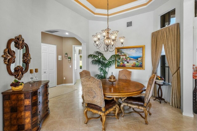 tiled dining space with a high ceiling, a raised ceiling, crown molding, and a chandelier