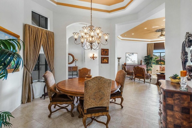 tiled dining area with ornamental molding, ceiling fan with notable chandelier, and a tray ceiling