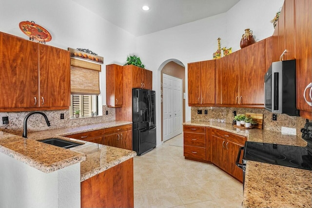 kitchen featuring black refrigerator, light stone countertops, kitchen peninsula, sink, and electric range oven