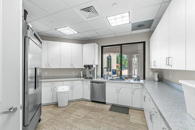 kitchen featuring light stone counters, stainless steel appliances, a drop ceiling, and white cabinets