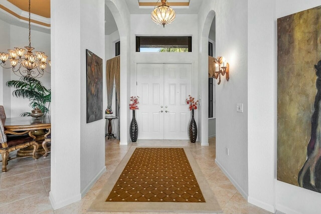 entrance foyer with a raised ceiling, a chandelier, a towering ceiling, ornamental molding, and light tile patterned flooring