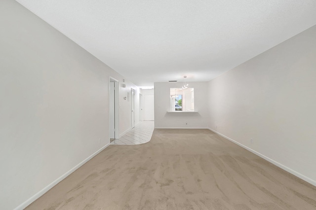 unfurnished room with light colored carpet, a notable chandelier, and a textured ceiling