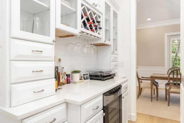 kitchen featuring white cabinetry, tasteful backsplash, wine cooler, crown molding, and light stone counters